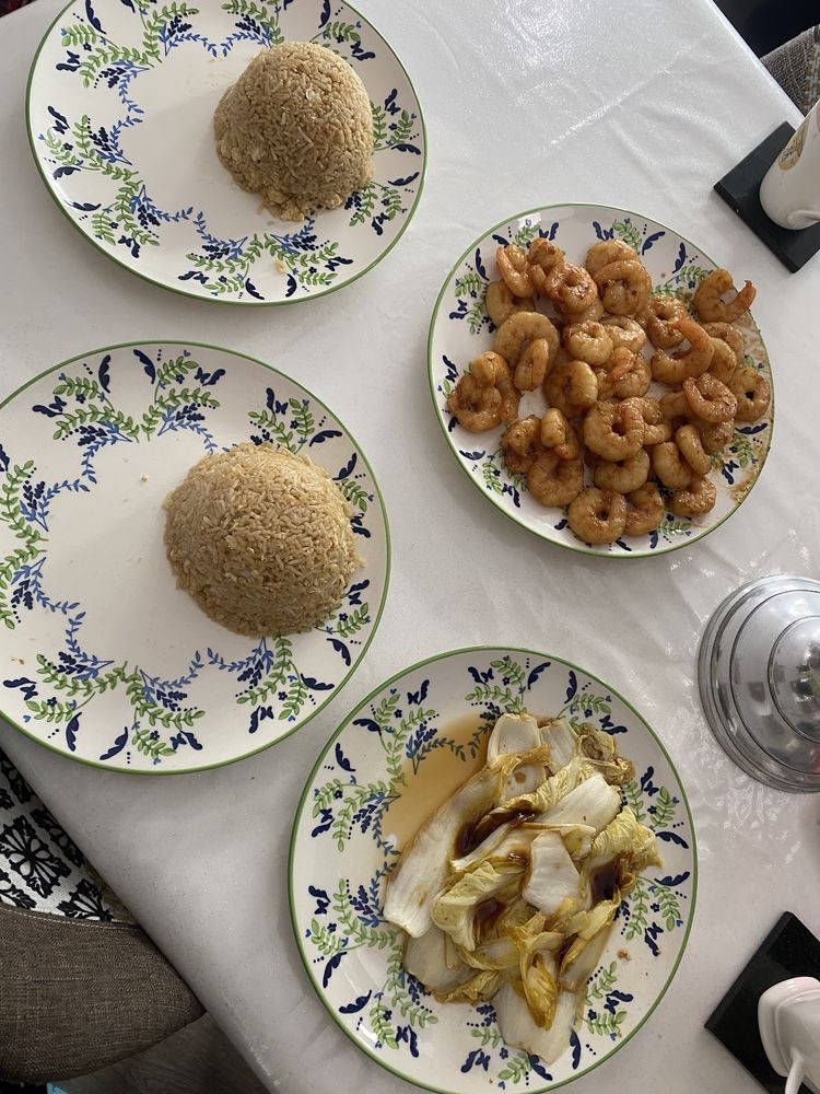 An overhead spread of small plates - rice domes, cooked prawns and greens - on a laid table